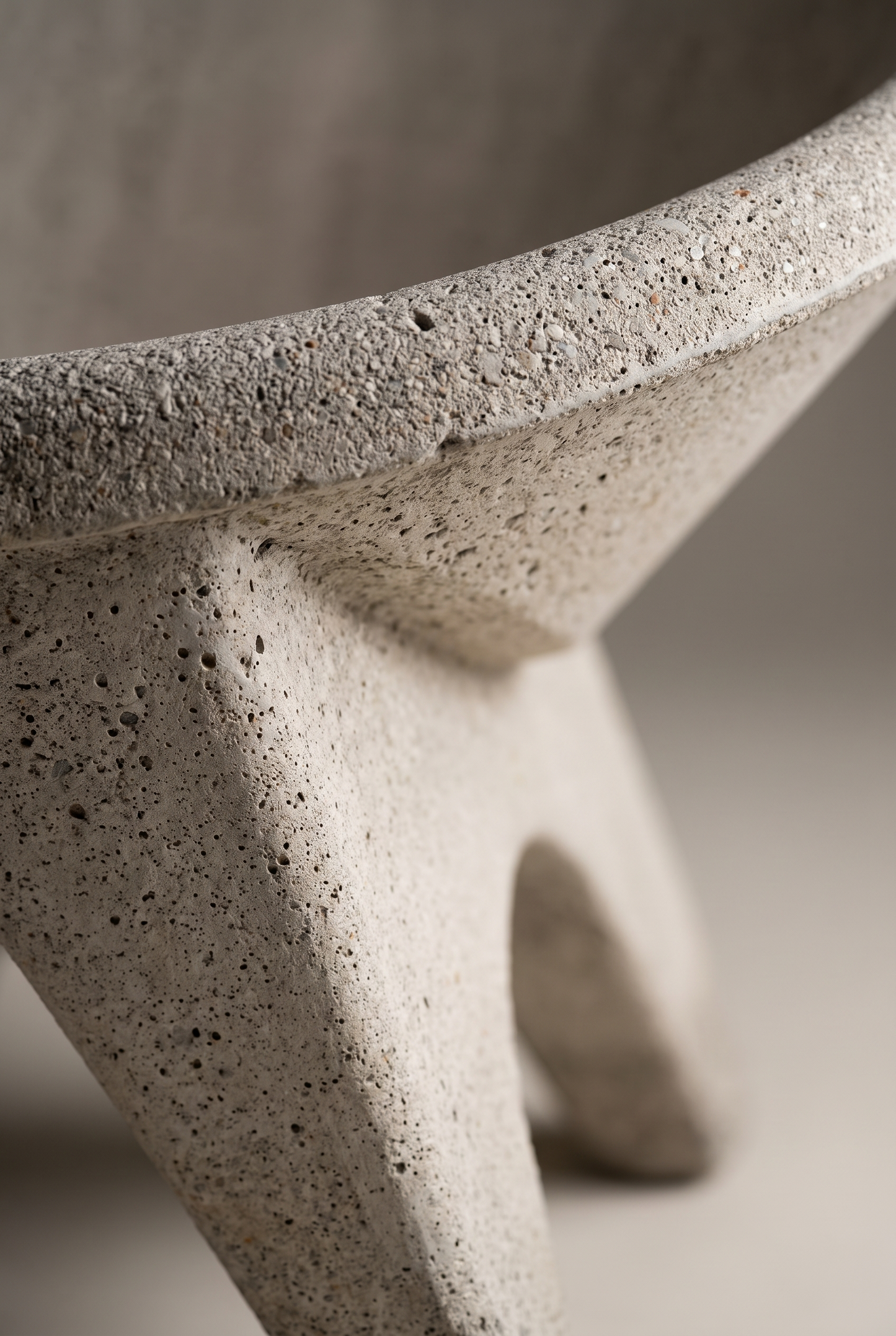 Close-up detail of a modern concrete stool with a textured, speckled stone-like finish and a sculptural three-legged base.