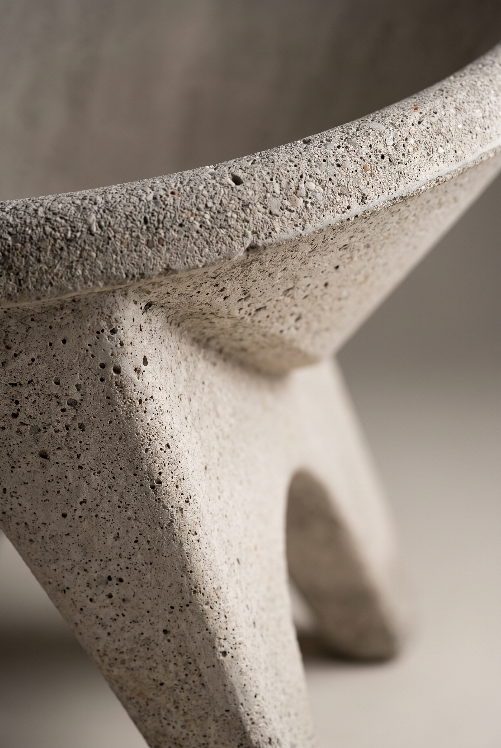 Close-up detail of a modern concrete stool with a textured, speckled stone-like finish and a sculptural three-legged base.